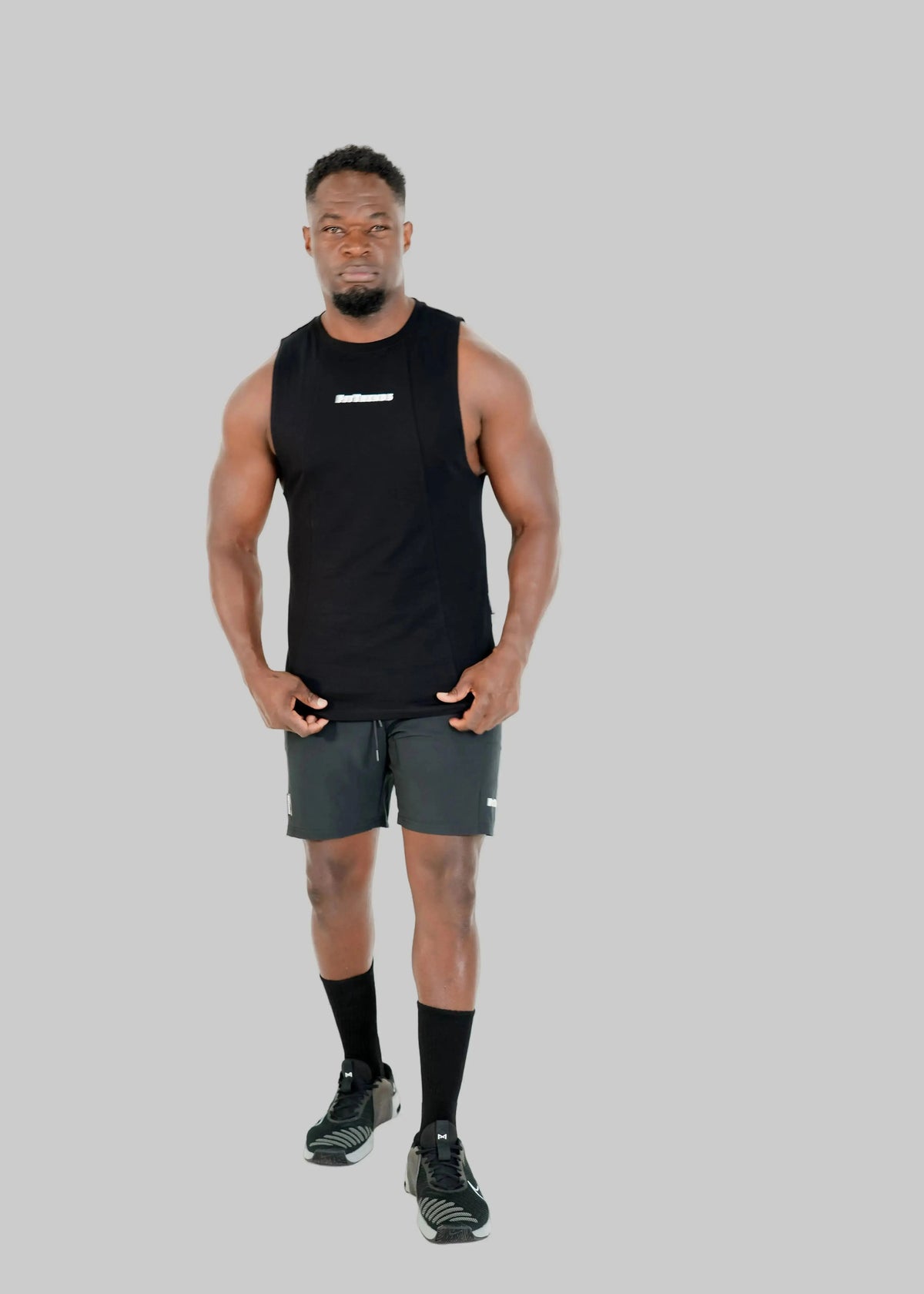 Man wearing a black sleeveless shirt and gray shorts on a white background
