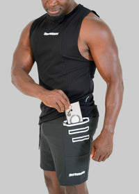 Man wearing a black sleeveless shirt and shorts with visible branding, holding a phone in his pocket.