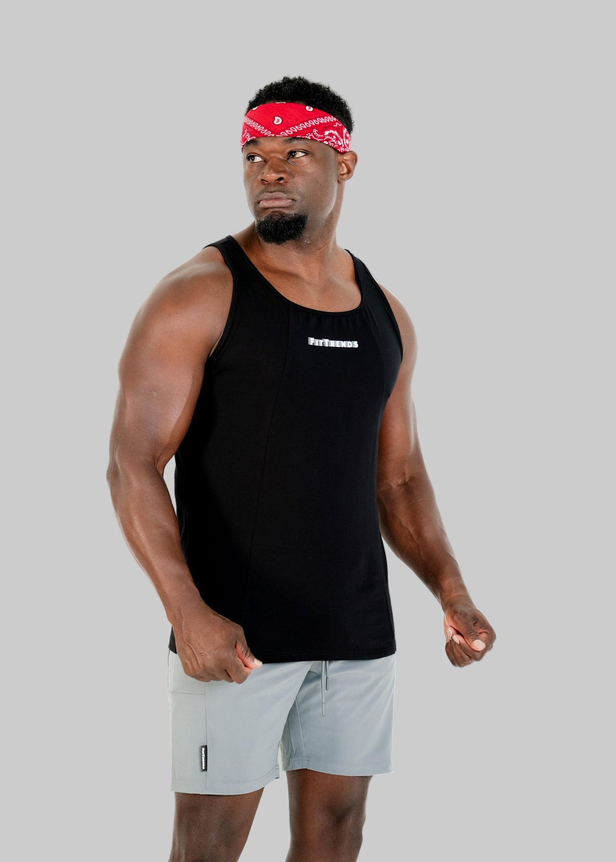 Man wearing a black tank top and light gray shorts with a red bandana on a white background