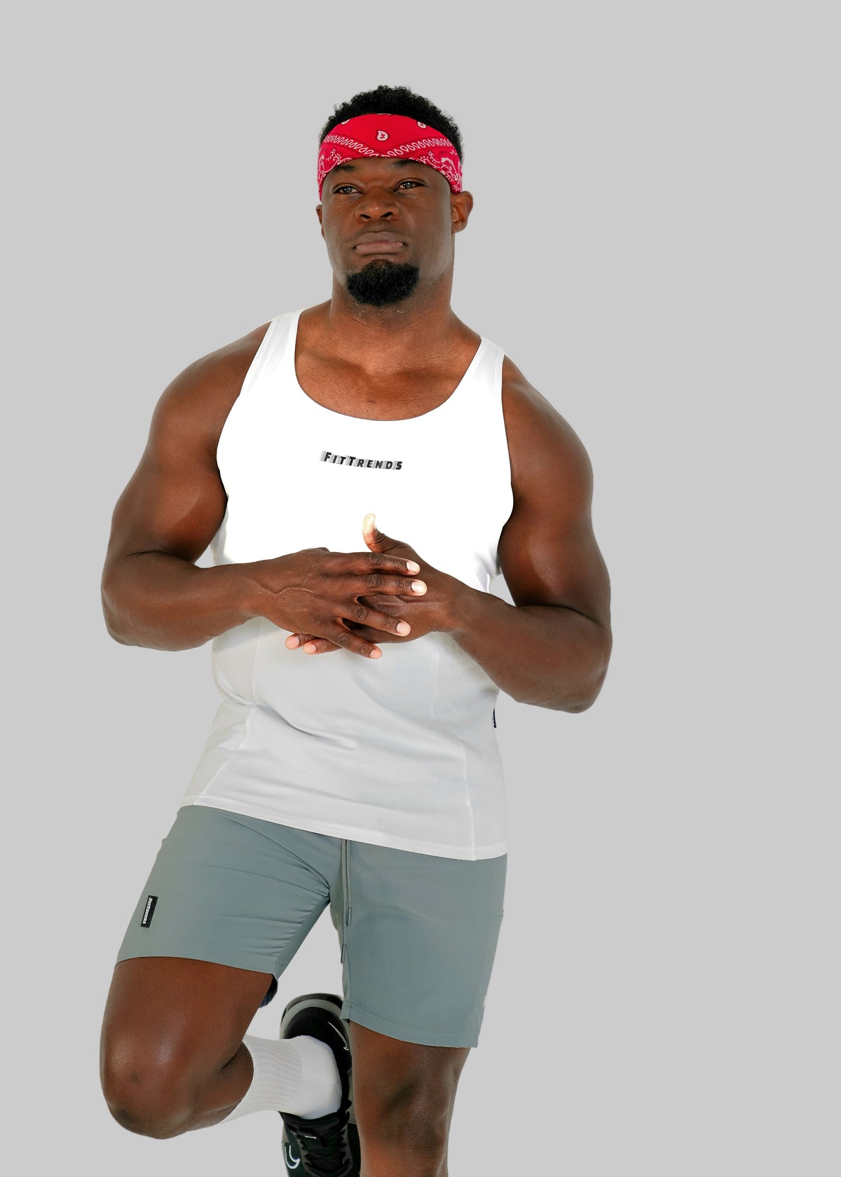 Man wearing a white tank top and gray shorts with a red bandana on a white background