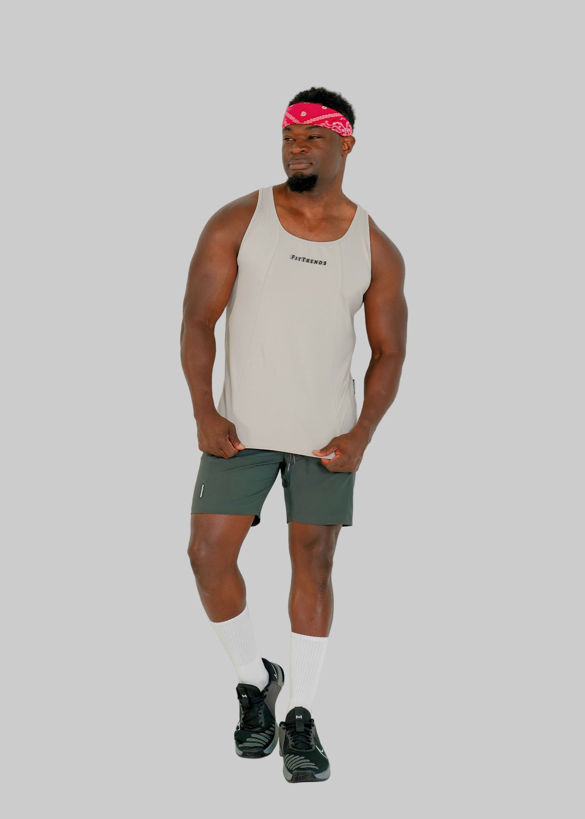 Man wearing a beige tank top and green shorts on a white background