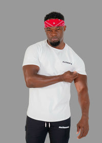 Man wearing a white t-shirt and black pants with a red bandana, standing against a plain background.