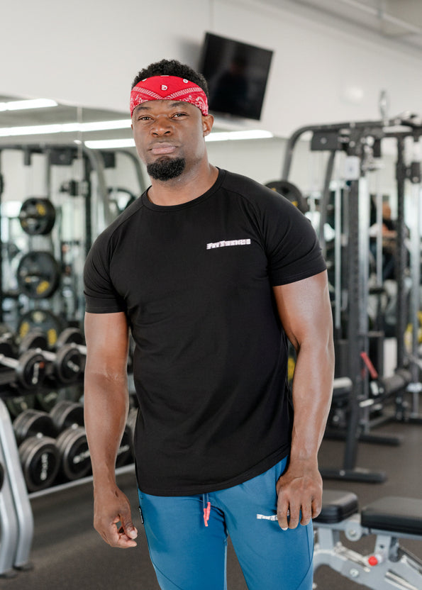 Man wearing a black t-shirt with a brand logo and blue pants on a white background