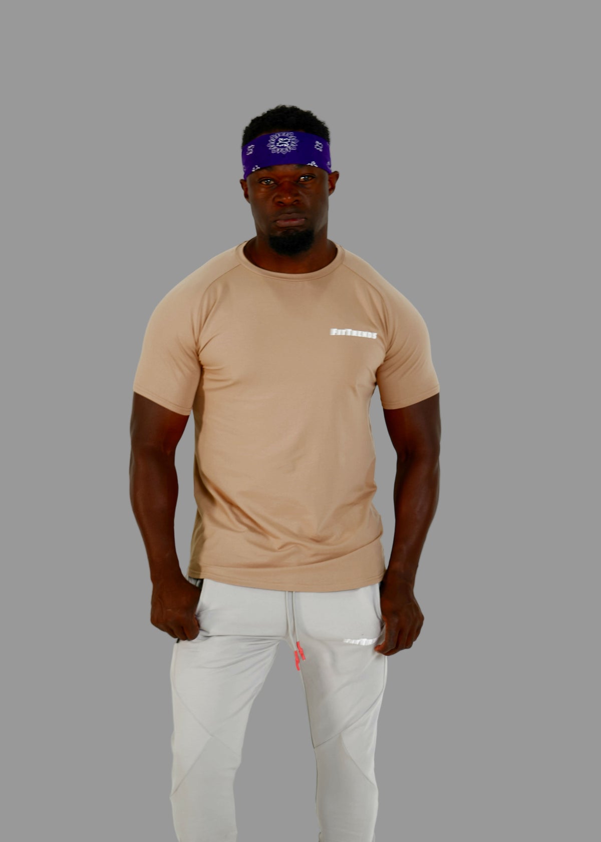 Man wearing a beige t-shirt and light gray pants against a white background