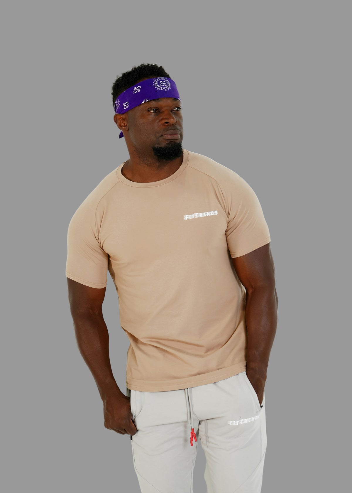 Man wearing a beige t-shirt with text and light gray pants against a white background