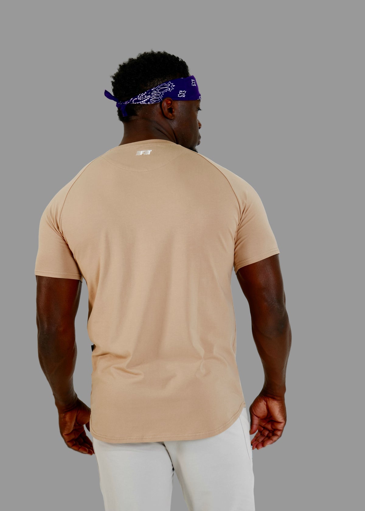 Man wearing a beige t-shirt and white pants on a plain background