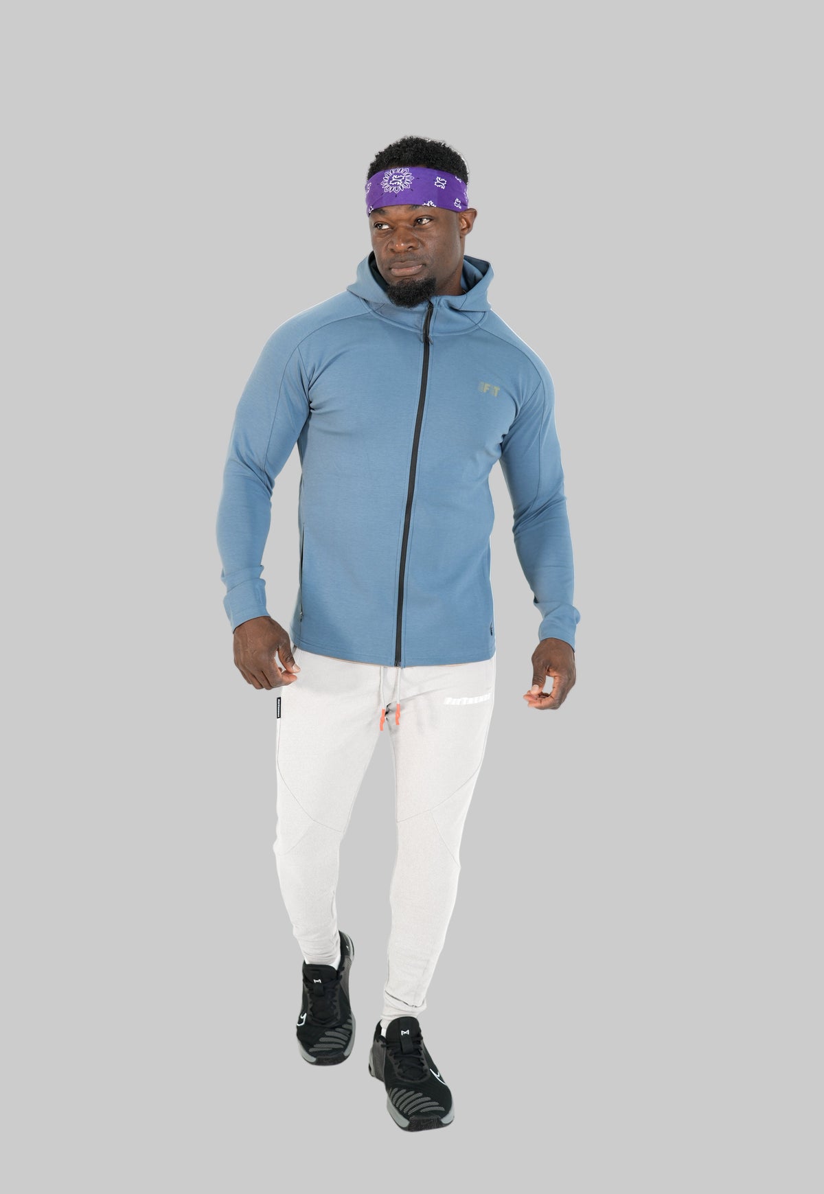 Man wearing a blue hoodie, white pants, and black shoes on a white background