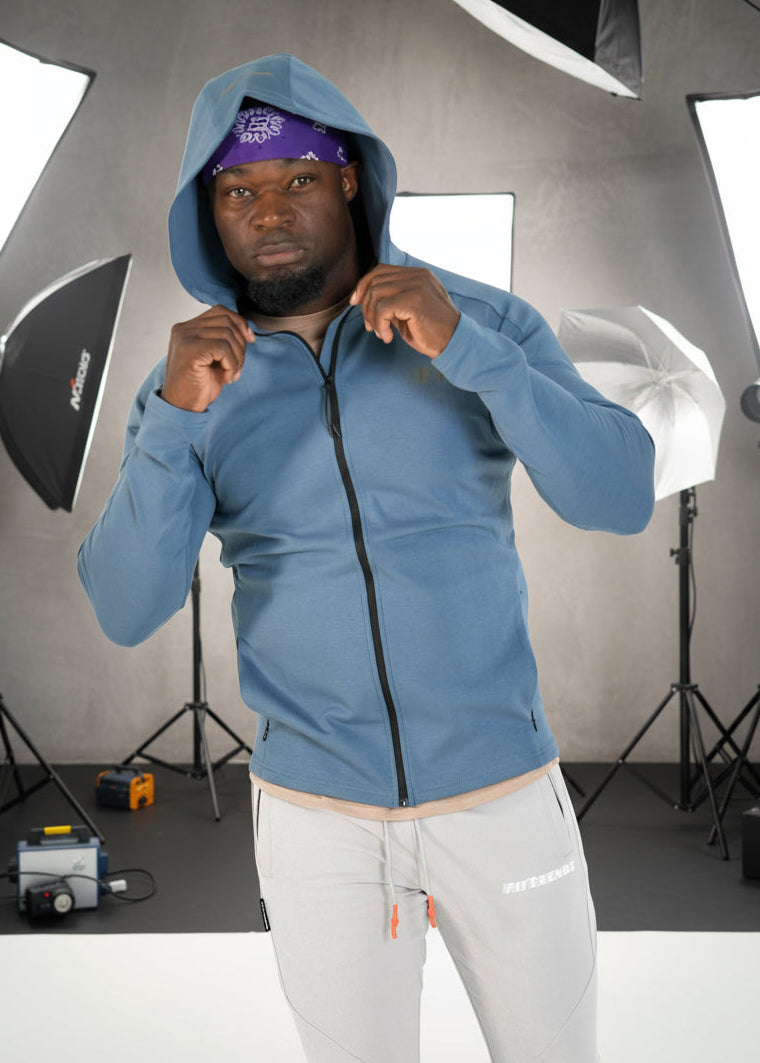 Person wearing a blue hoodie and white pants on a white background