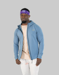 Man wearing a blue jacket, beige shirt, and white pants on a white background