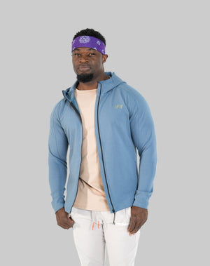 Man wearing a blue jacket, beige shirt, and white pants on a white background