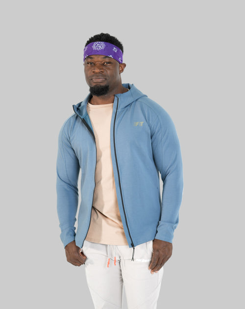 Man wearing a blue jacket, beige shirt, and white pants on a white background