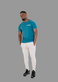 Man wearing a teal t-shirt and white pants on a white background
