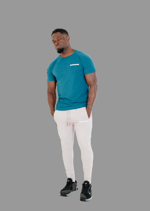 Man wearing a teal t-shirt and white pants on a white background