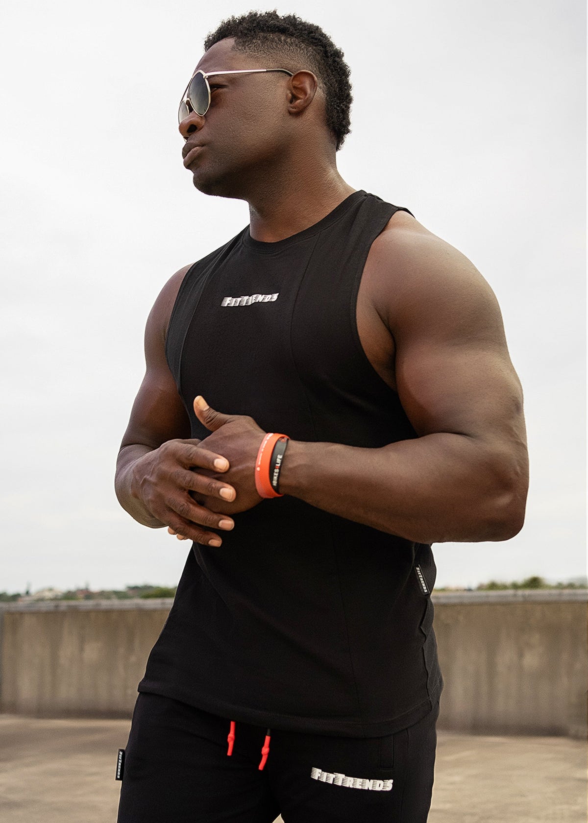Man wearing a black sleeveless shirt and pants with visible branding, standing outdoors.