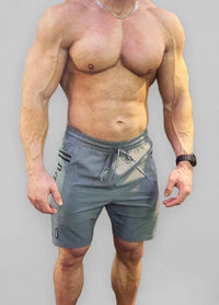 A muscular man wearing gray athletic shorts with a drawstring waist and side pockets, shown from the chest down against a plain light gray background.