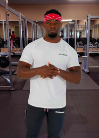 Man in a gym wearing a white t-shirt and black pants with a red bandana.