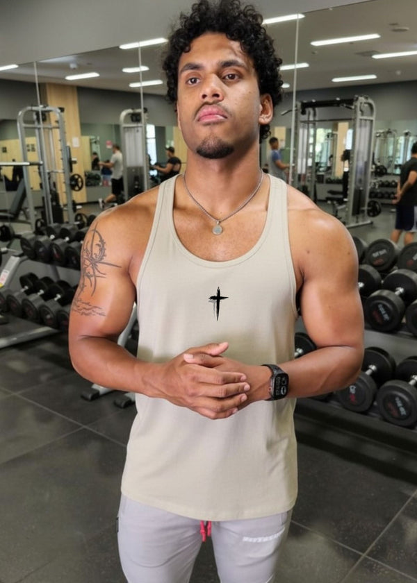 Man in a gym wearing a beige tank top and light gray pants.
