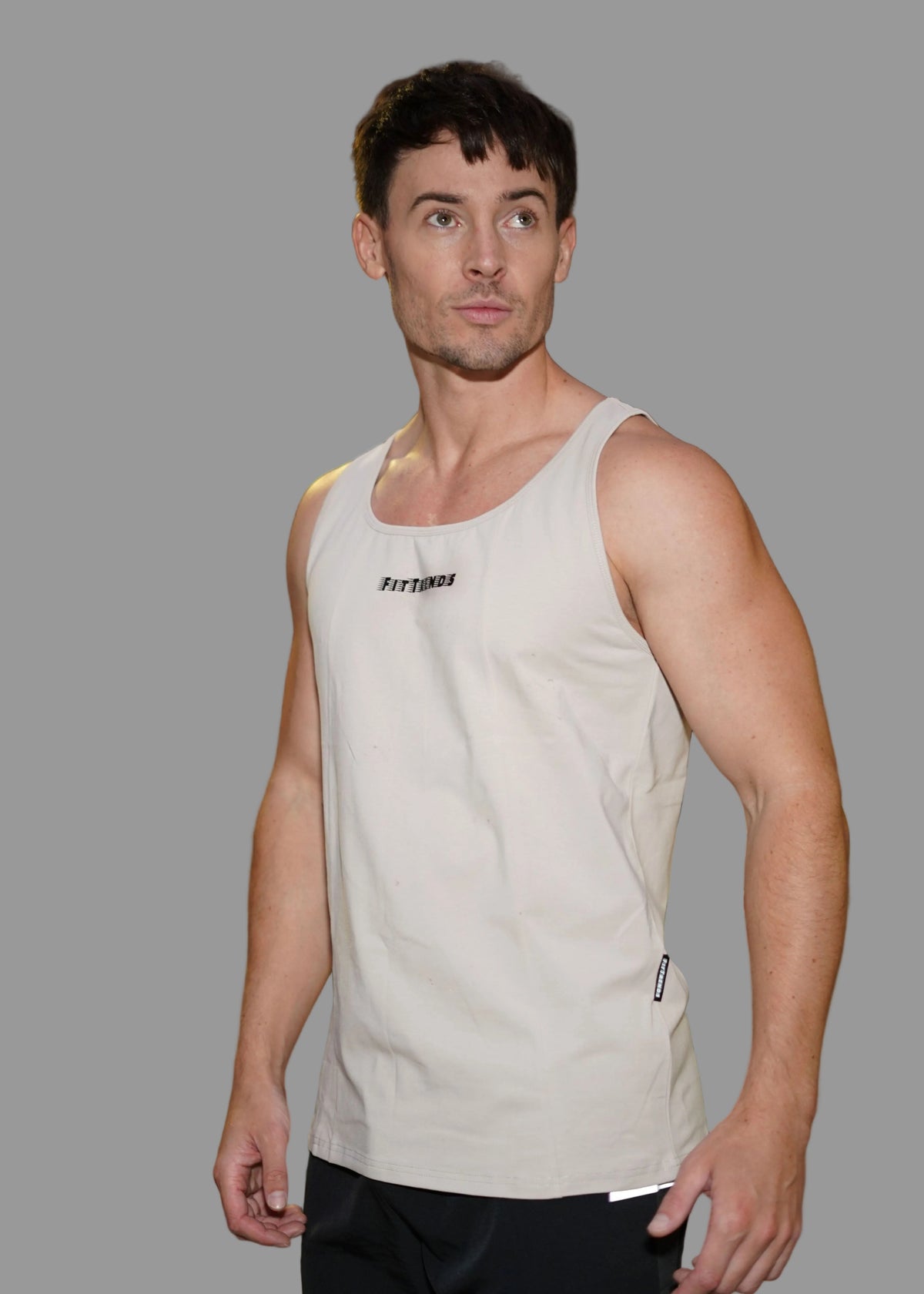 Man wearing a beige tank top with a brand logo at night.