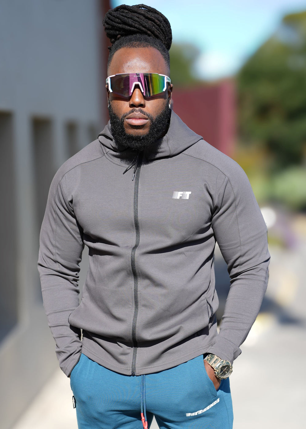 Man wearing a gray jacket and blue pants standing on a street.