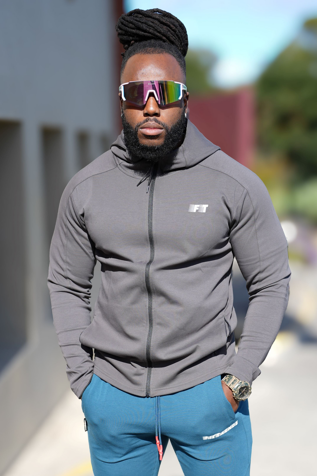 Man wearing a gray hoodie and blue pants with reflective sunglasses outdoors.