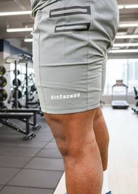 Person wearing gray shorts with 'FitFrends' branding in a gym setting