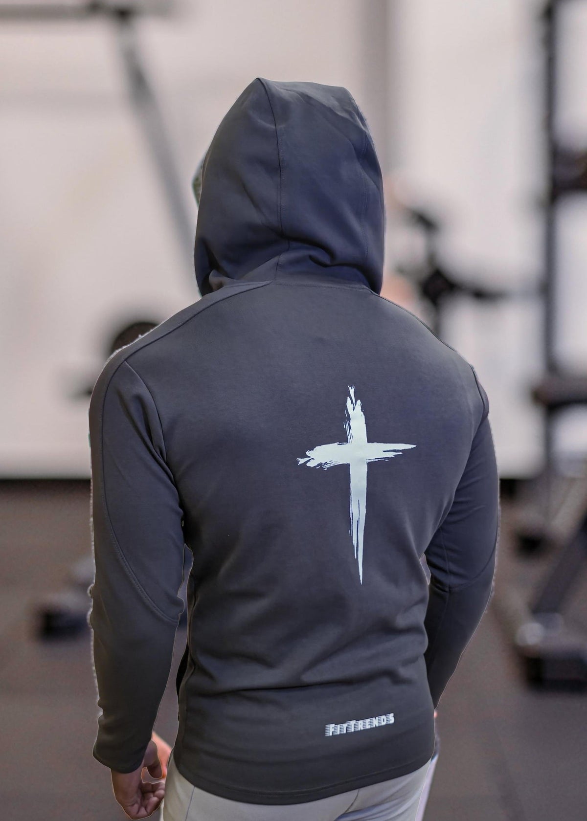 Person wearing a dark hoodie with a white logo on the back, standing in an indoor setting.