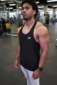Man wearing a black tank top with a logo in a gym setting